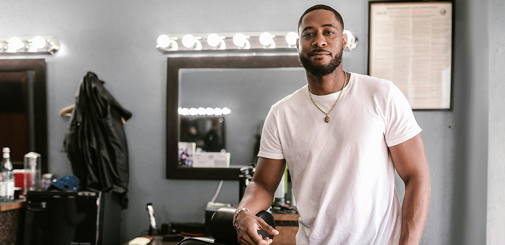 Barber in a white T-shirt standing beside a barber chair